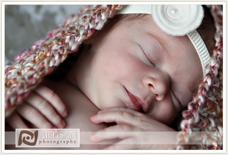 newborn baby girl in cocoon on rustic floor smiling