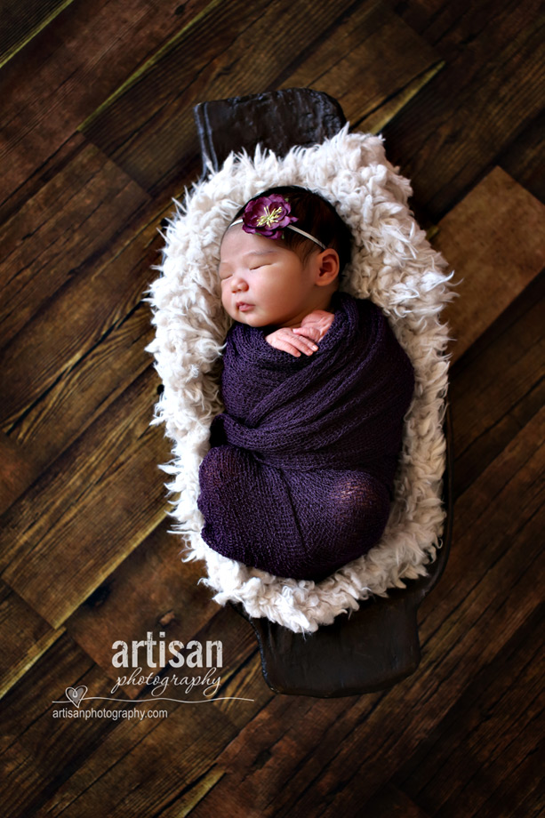 newborn baby girl in purple wrap with a purple flower on hwer hair