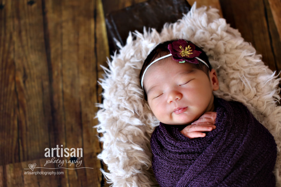 baby girl photo wrapped in purple wrap with cute flower in the hair.