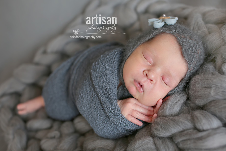 baby girl laying on blanket with flower hat on grey chunky blanket