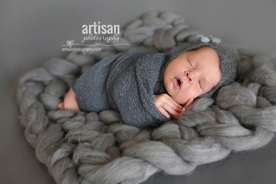 baby girl laying on blanket with flower hat on grey chunky blanket