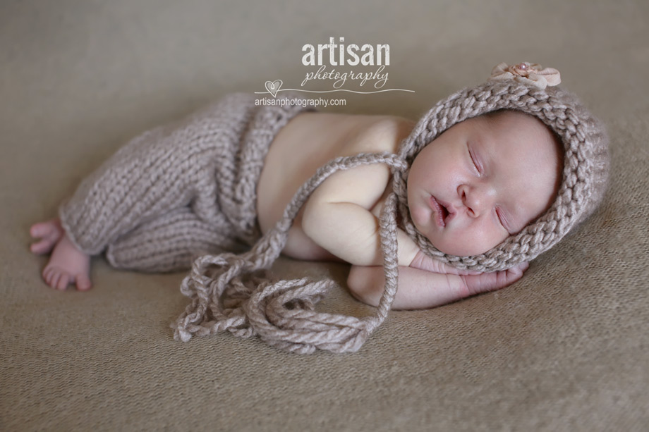 baby girl laying on blanket with flower headband and beije pants and hat