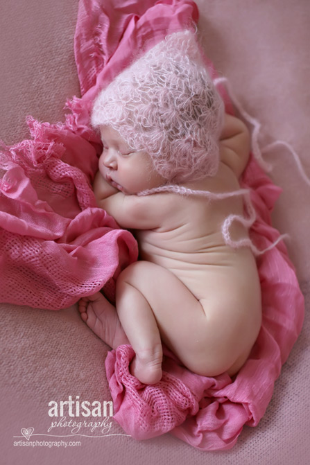 baby girl laying on blanket with pink hatin dusty pink background at the artisan studio in carlsbad