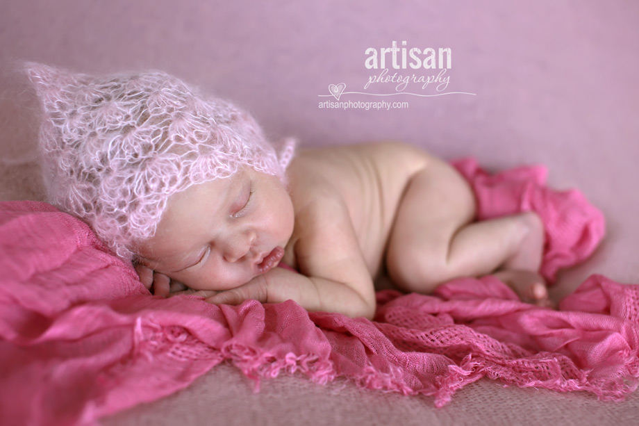 baby girl laying on blanket with flower headband in dusty pink background at the artisan studio