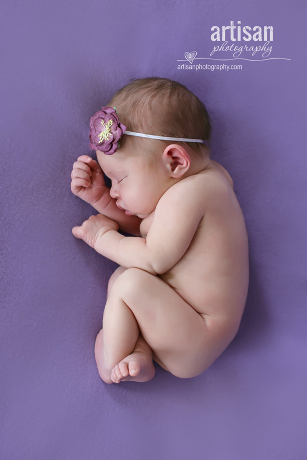 baby girl laying on blanket with flower headband in lavander background at the artisan studio