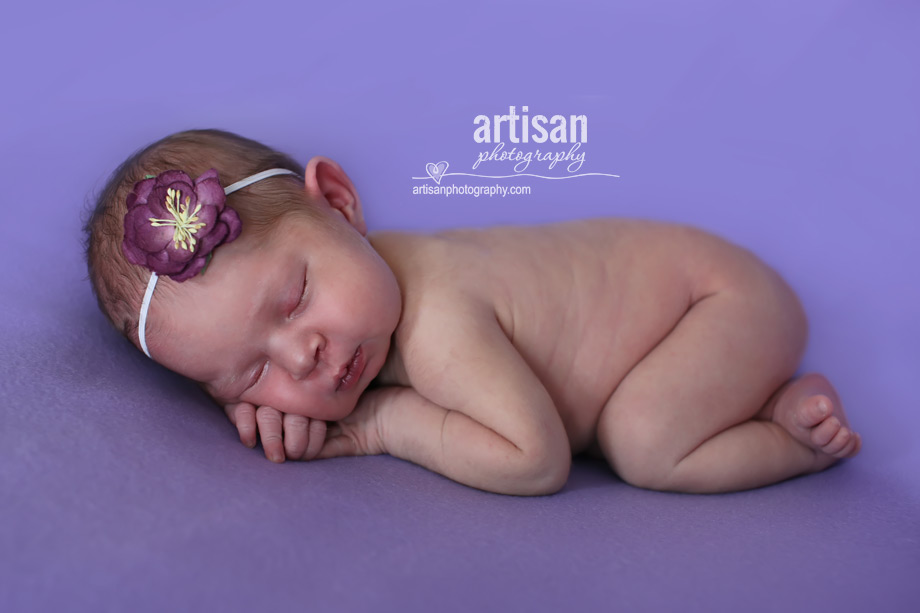 baby girl laying on blanket with flower headband in lavander background at the artisan studio