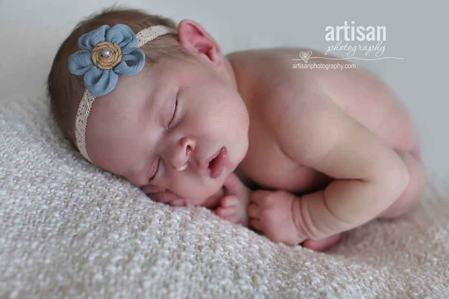 baby girl laying on blanket with flower headband in white background at the artisan studio