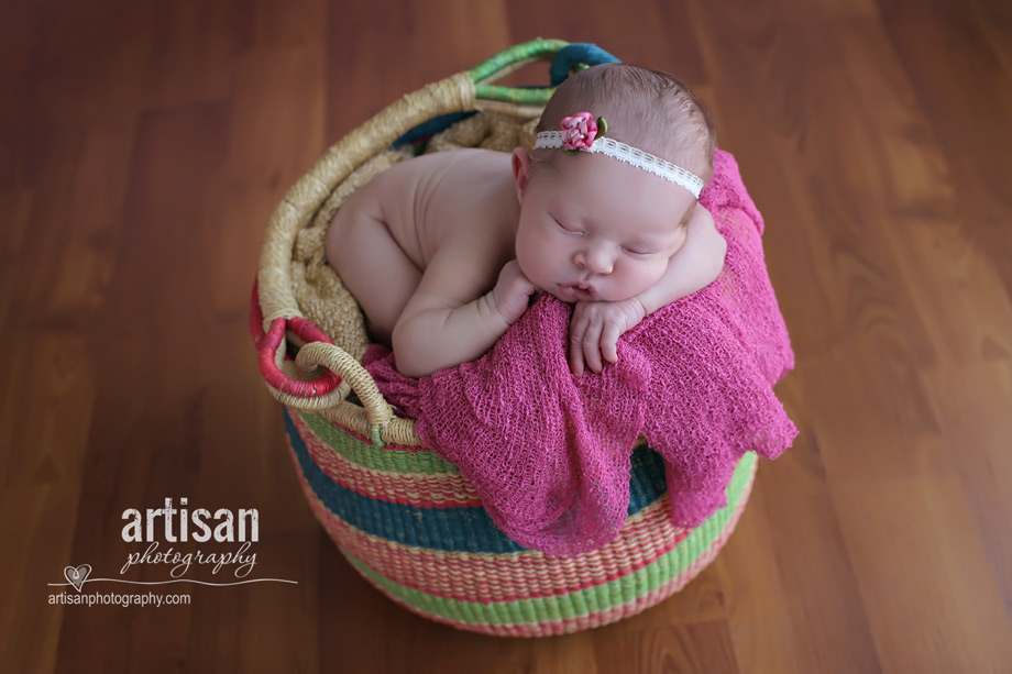 baby girl in african basket with flower headband in dusty pink background at the artisan studio