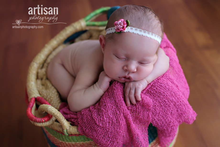 baby girl laying in african weaved basket with flower headband in dusty pink background at the artisan studio