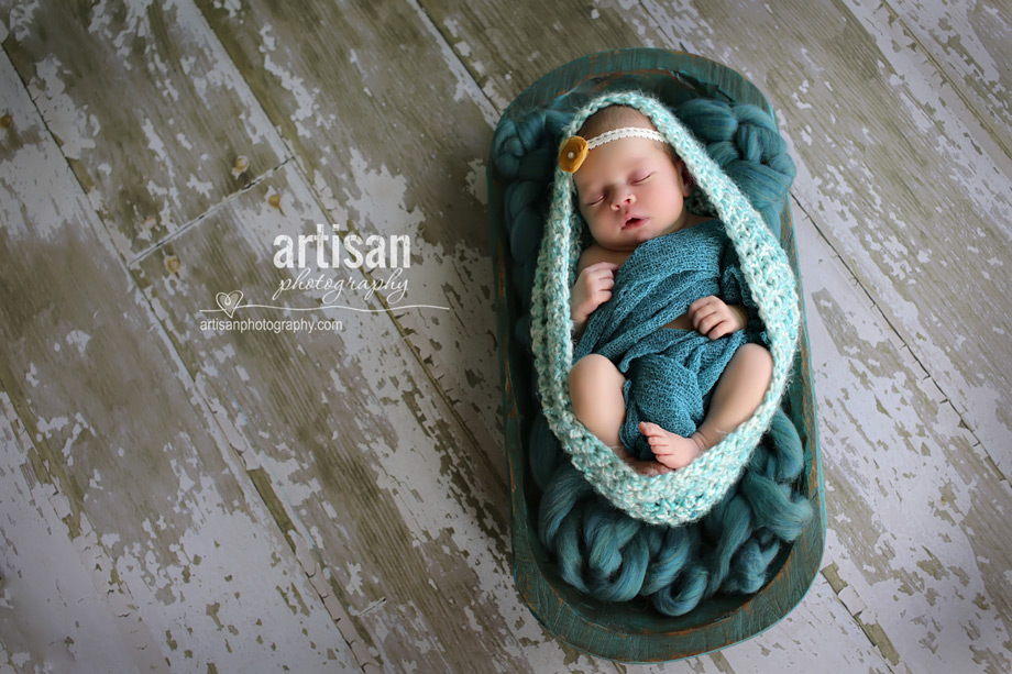 baby girl laying on blanket with flower headband in turquoise background at the artisan studio