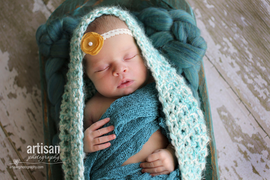 baby girl laying on turquoise tray with flower headband in dusty pink background at the artisan studio