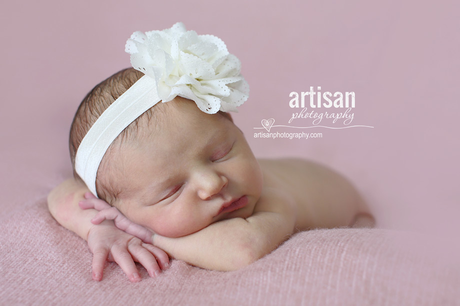 newborn baby girl photo at our Carlsbad studio in California with a big white flower band in dusty pink background