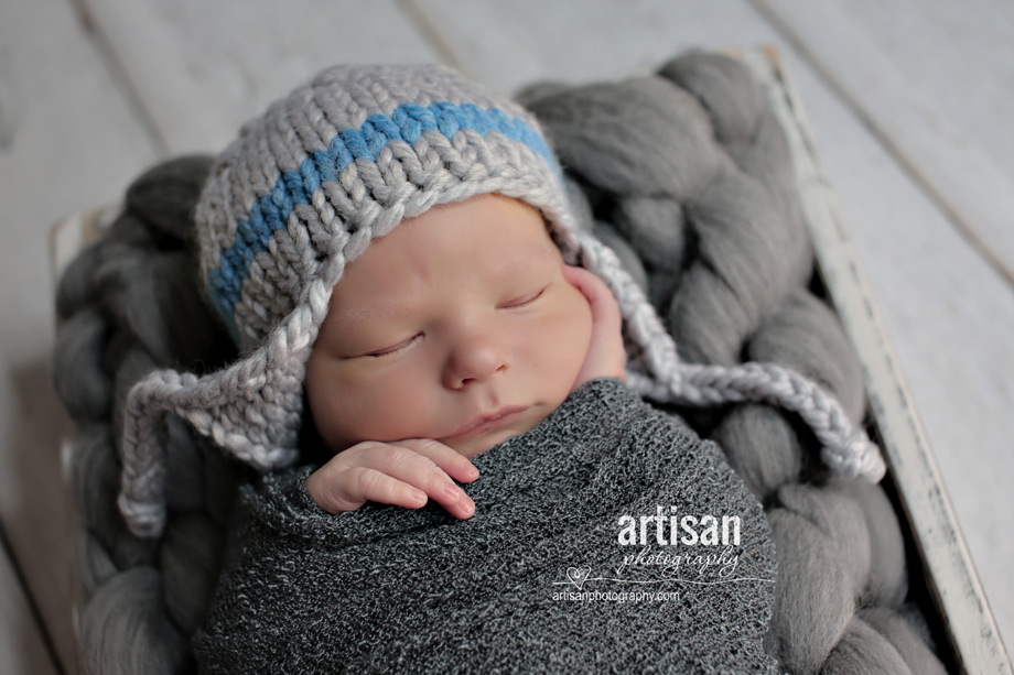 professional photo of newborn baby on grey background and a blue and grey hat