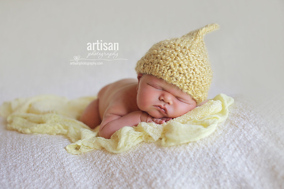 newborn baby boy photo laying on a cream color blanket wearing a yellow elf hat in Carlsbad California