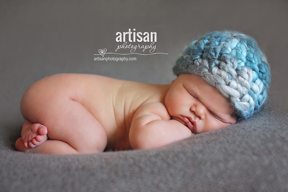 newborn baby boy photo laying on a grey blanket with a blue chunky hat in Carlsbad California