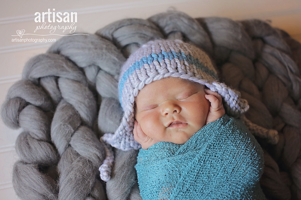 newborn baby boy photo laying on a chunky grey blanket smiling in Carlsbad California 