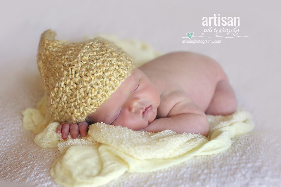 newborn baby boy laying on a cream blanket with an yellow elf hat in Carlsbad California