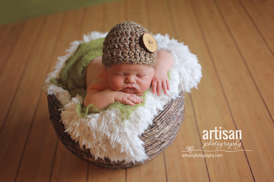 newborn baby boy laying on a brown wicker basket and a brown button hat in Carlsbad california