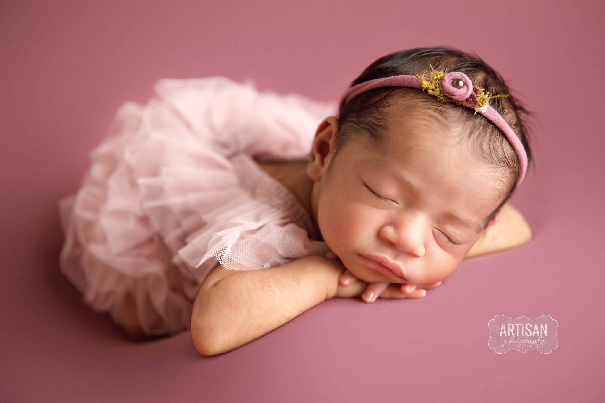 Newborn baby girl with a light pink dress, sleeping with head resting on hands